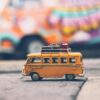 Close-up of a toy Volkswagen van with luggage, set against a colorful street backdrop, evoking summer travel vibes.